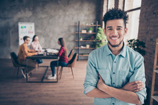 young man smiling with group of young adults in background at a table