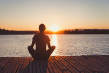 Woman meditating at a lake on a pier.
