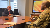 Soldier and business man meeting and sitting across from one another at an office desk.